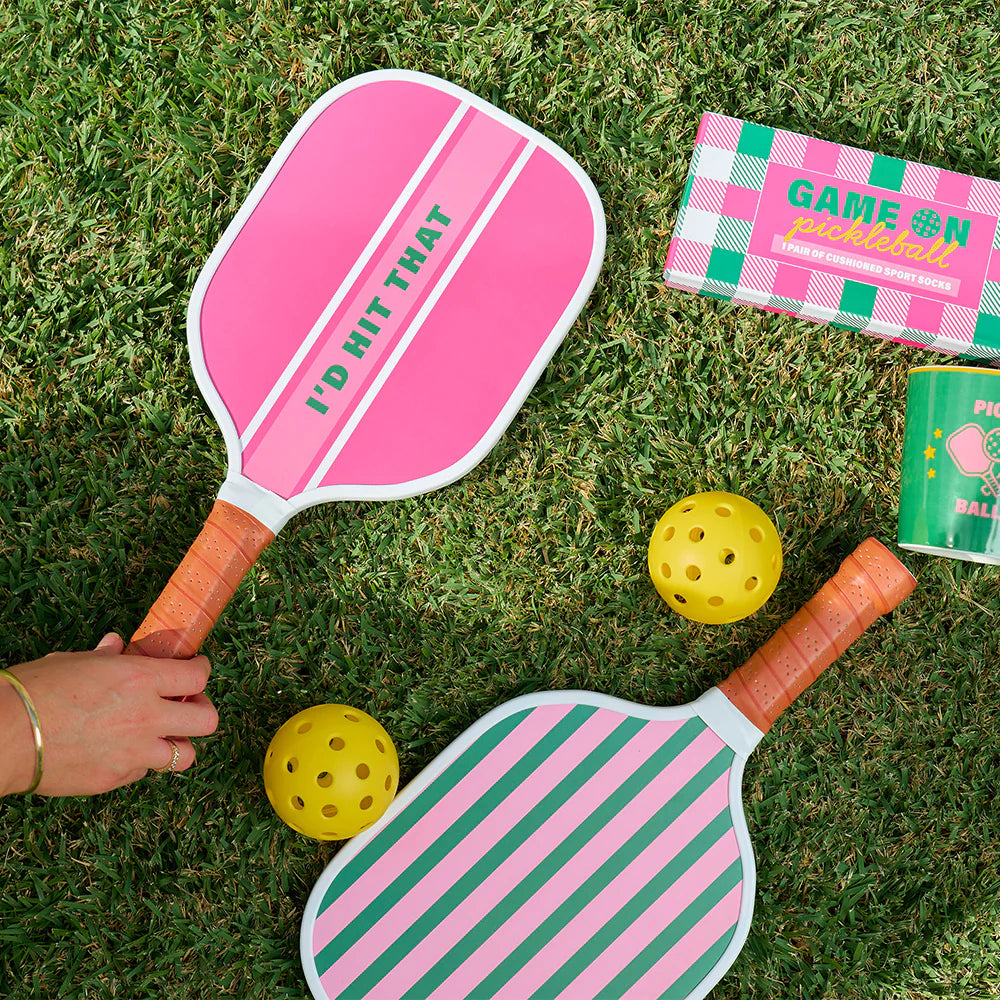 Pink and green pickleball paddles with yellow balls on grass