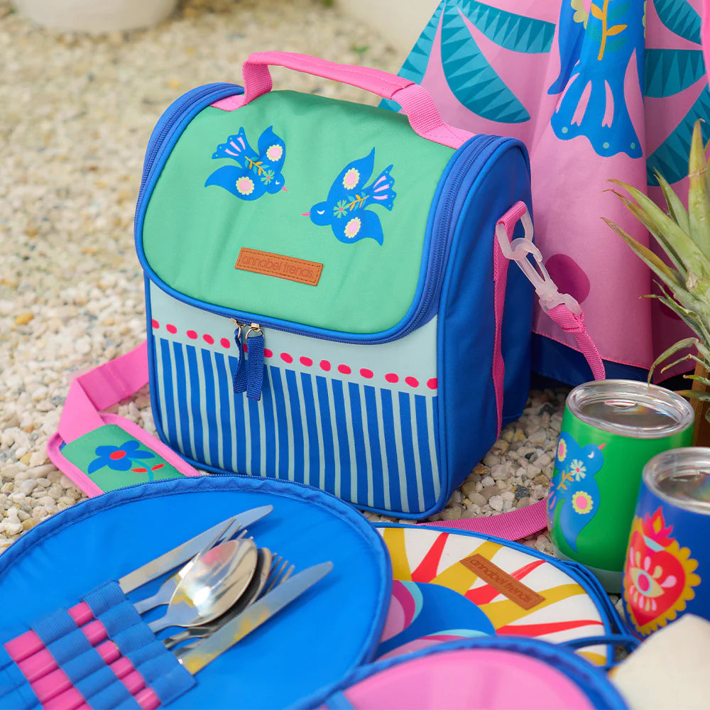 Colorful picnic set with a lunch bag, plates, and cutlery on a textured surface.