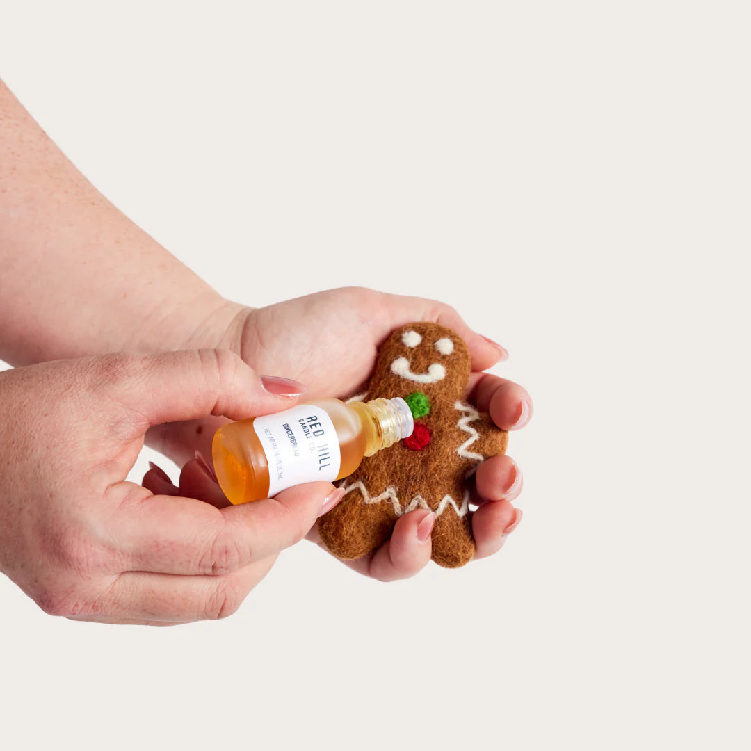 Hand holding a small scent bottle with a gingerbread man felt design on a plain background
