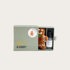 Box containing a gingerbread man air freshener and a bottle of fragrance oil on a light gray background