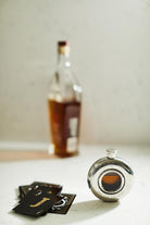 Silver flask with a bottle and playing cards on a light surface