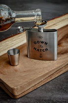 Stainless steel flask with 'Down The Hatch' engraving on a wooden surface.