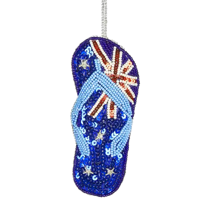 A sequin decoration in the shape of an Australian thong with a colorful design, including blue, red, white, and green elements, and adorned with sparkling stones.