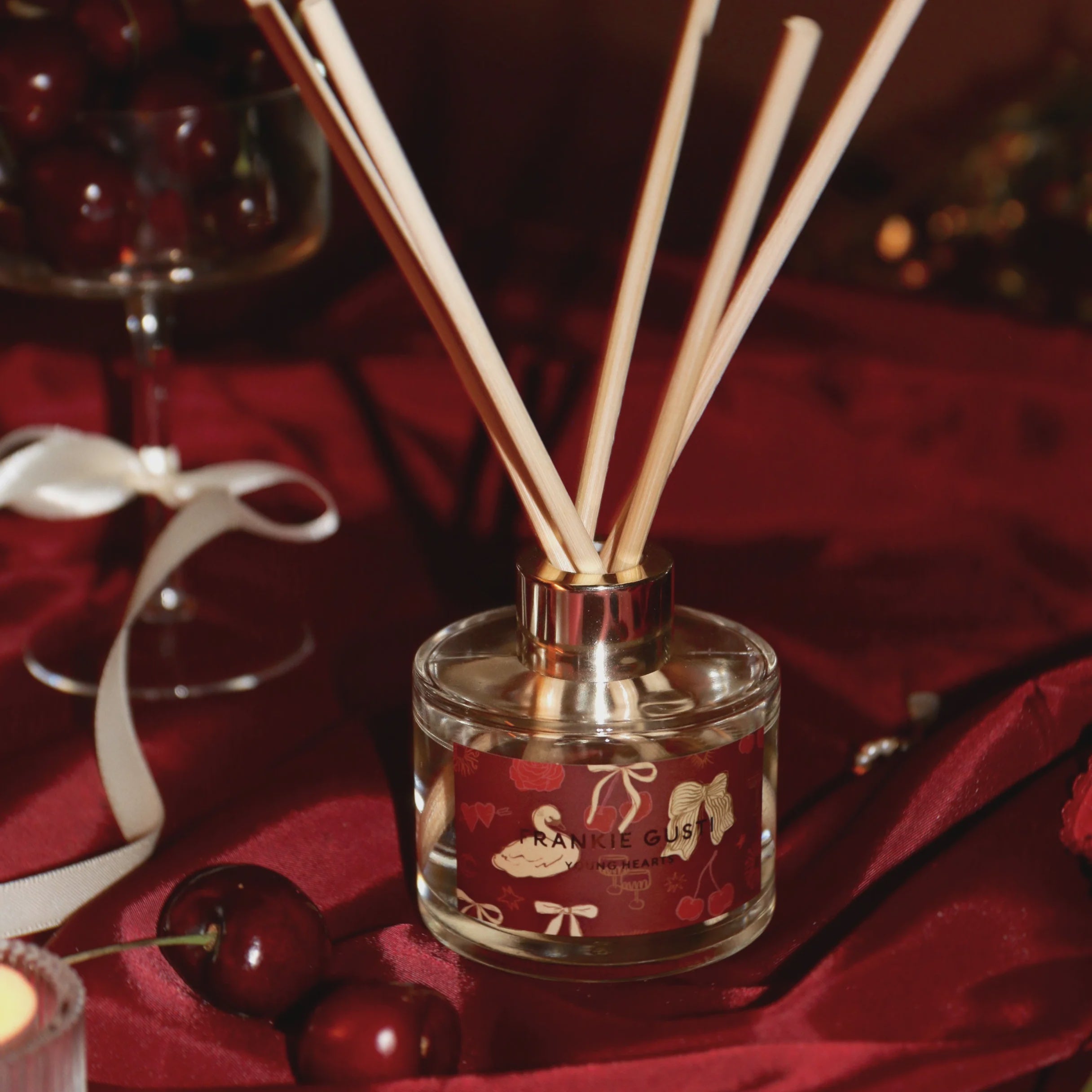 Reed diffuser with wooden sticks on a red fabric background inspired by Cherries