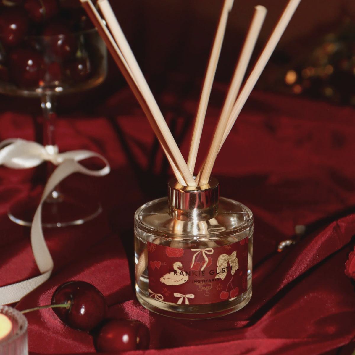 Reed diffuser with wooden sticks on a red fabric background inspired by Cherries
