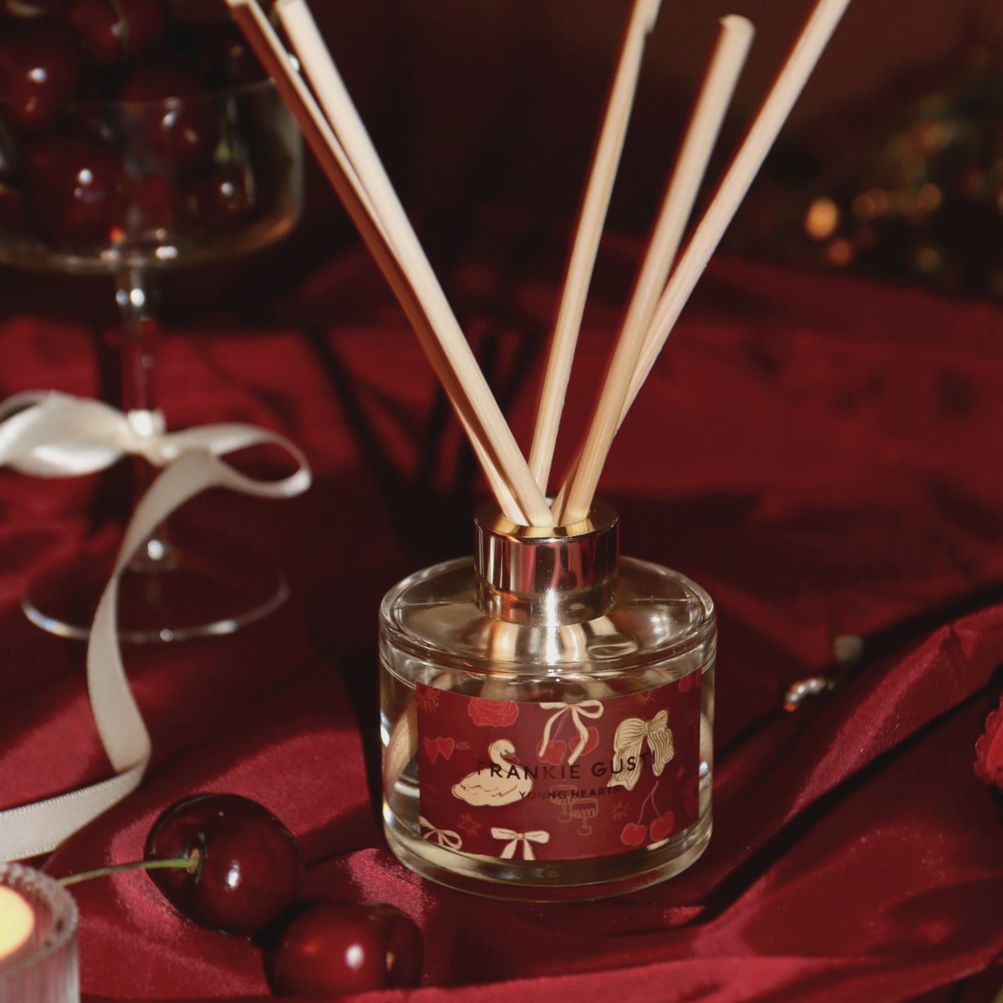 Reed diffuser with wooden sticks on a red fabric background inspired by Cherries