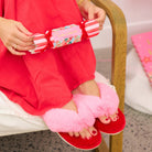 Person wearing pink fuzzy slippers holding a red and white striped bon bon full of bath confetti
