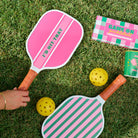 Pink and green pickleball paddles with yellow balls on grass