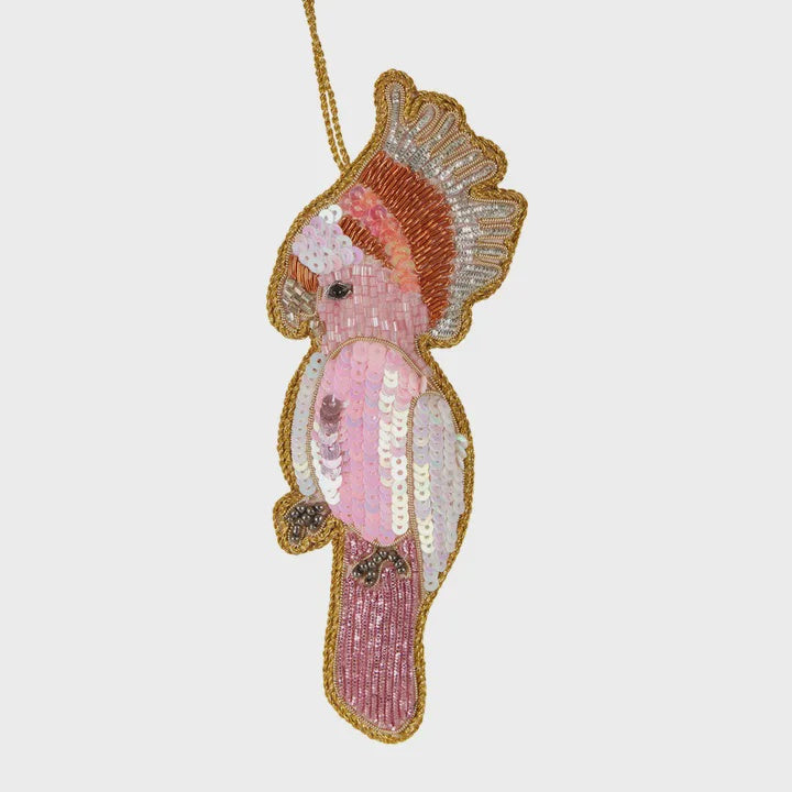 A sequinned decoration in the shape of a galah bird, predominantly pink and white, with gold accents and lightweight beading.