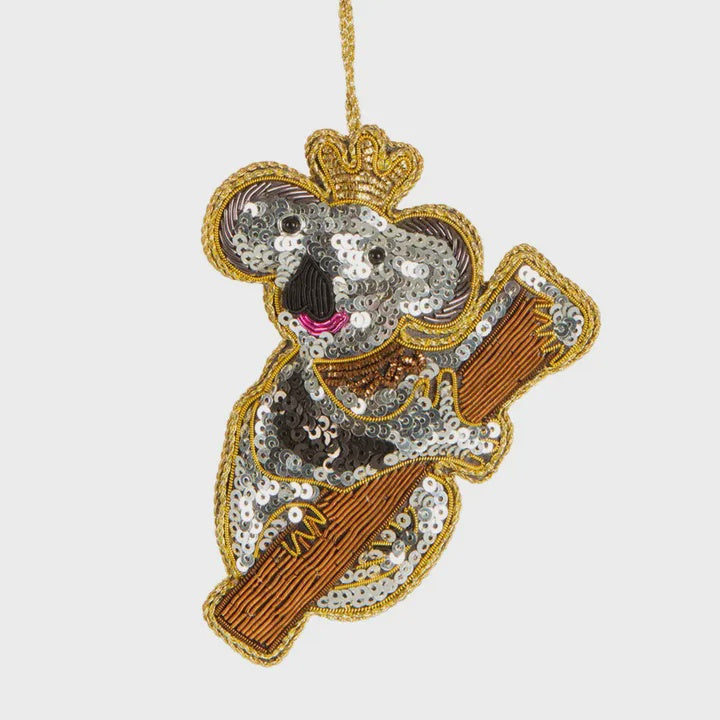 A sequinned decoration of a koala holding a musical instrument, with a crown on its head and a sequin-covered body.
